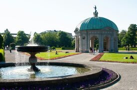 Brunnen mit Fontäne vor einem Pavillon mit Kuppel in einem Park