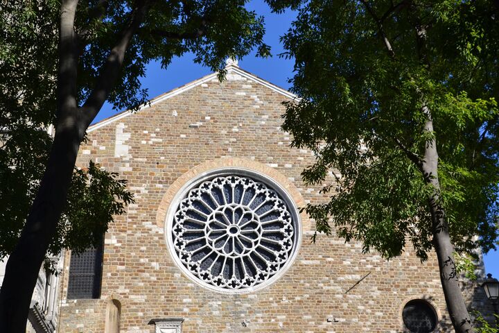 Eine Kirche aus Ziegelsteinen mit einem großen runden Fenster hinter zwei Bäumen