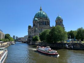 Auf dem Bild sieht man den Berliner Dom und die Spree, auf der ein Ausflugsschiff fährt.