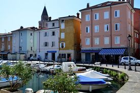 Bunte Häuser und kleine Boote im Hafen von Muggia an einem sonnigen Tag.