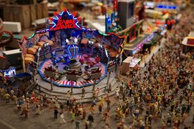 Miniatur einer Menschenmenge auf einem Jahrmarkt vor dem Breakdancefahrgeschäft