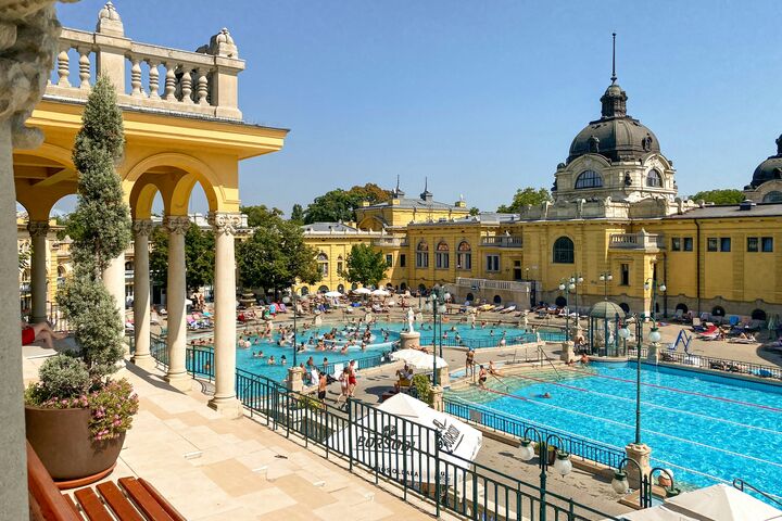 Ein Outdoor-Schwimmbad mit zwei Becken, vielen Menschen und historischen Gebäuden