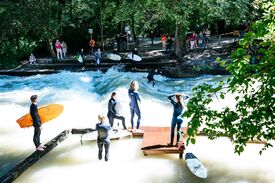 Menschen mit Surfboards am Ufer eines schmalen Gewässers mit einer starken Welle