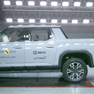 Das Foto zeigt ein hellgraues Auto von der Seite, das gerade im Zuge eines Crashtests frontal gegen ein Hindernis prallt.