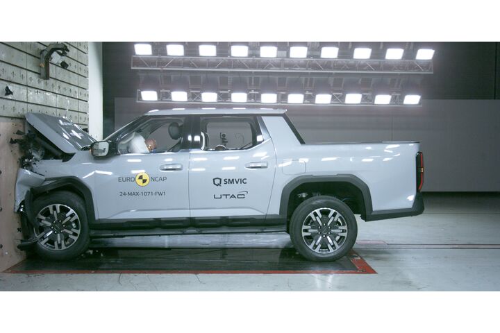 Das Foto zeigt ein hellgraues Auto von der Seite, das gerade im Zuge eines Crashtests frontal gegen ein Hindernis prallt.