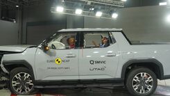 Crashtest von einem weißen großen Pickup. Die Motorhaube ist stark eingedrückt und kaputt. Das Fahrzeug steht in einer Testhalle.
