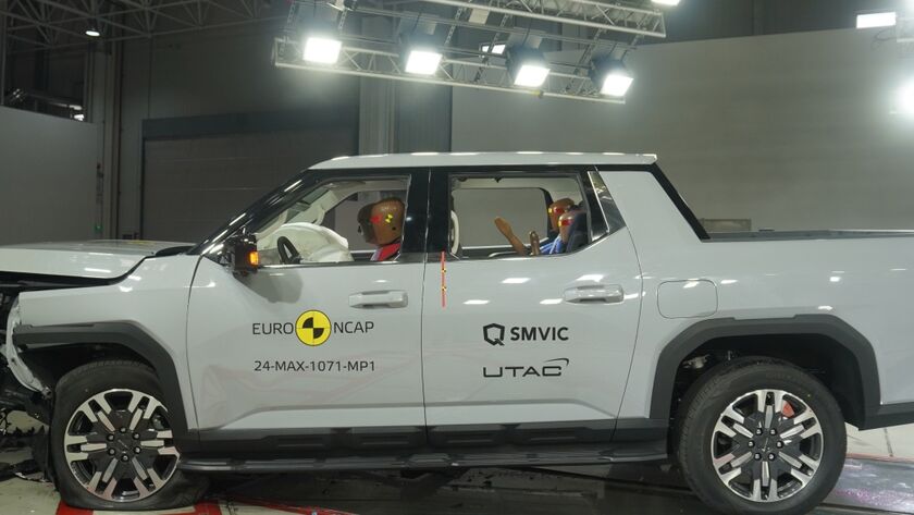 Crashtest von einem weißen großen Pickup. Die Motorhaube ist stark eingedrückt und kaputt. Das Fahrzeug steht in einer Testhalle.