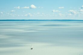 der hellblaue Plattensee mit einem kleinen Segelboot und einer Küste am Horizont