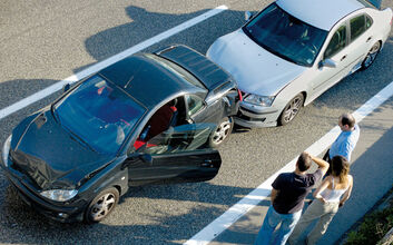 Luftaufnahme von 2 PKW, drei Menschen stehen ratlos daneben. Das hintere Auto ist leicht beschädigt, das vordere Fahrzeug hat eine geöffnete Fahrertüre, die Stoßstange hinten ist eingedrückt.