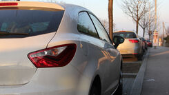 Mehrere Autos parken am Straßenrand, dazwischen sind kleine Grünflächen mit einem Baum.
