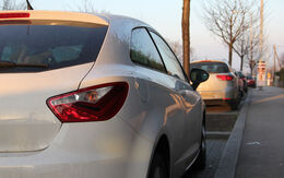 Mehrere Autos parken am Straßenrand, dazwischen sind kleine Grünflächen mit einem Baum.