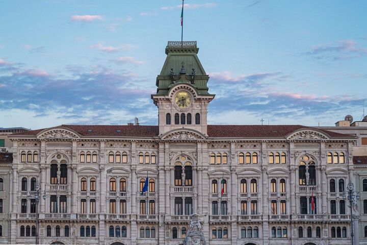Neoklassizistisches Gebäude mit Uhrturm in Triest vor blauem Himmel in der Dämmerung.