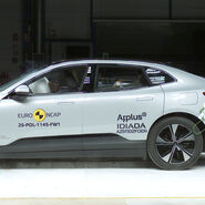 Das Foto zeigt ein hellgraues Auto von der Seite, das gerade im Zuge eines Crashtests frontal gegen ein Hindernis prallt.