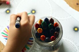 Stifte und eine Kinderhand, die etwas anmalt