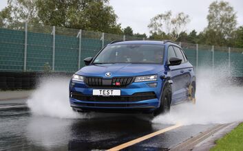 Fahrendes blaues Auto auf nasser Fahrbahn.