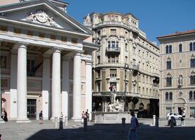 Das Börsengebäude in Triest mit Säulen und einer Uhr und anderen Gebäuden im Hintergrund