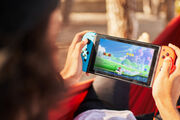 Nicht erkennbare Person mit einer Verschlusskappe, die Videospiele auf einer tragbaren Konsole spielt, während sie auf Hängematte hängt.