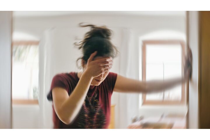 Verschwommenes Foto einer Frau, die unter Schwindel oder Benommenheit leidet, ausgelöst durch eine Erkrankung des Gehirns oder des Innenohrs.