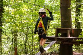 Ein Kind, das gesichert über ein Hindernis in einem Kletterpark geht