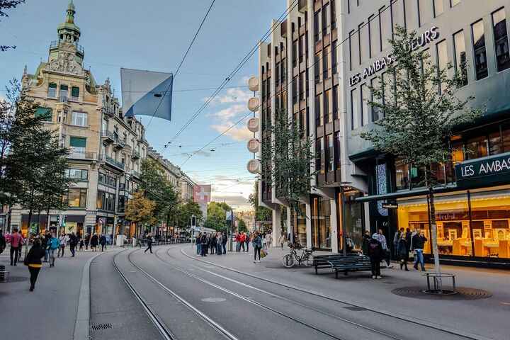Eine Einkaufsstraße mit Straßenbahnschienen und Menschen, die flanieren