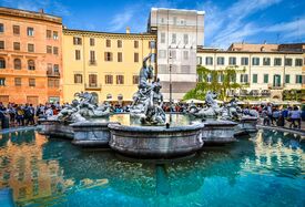 Ein Brunnen mit vielen Figuren auf einem großen Platz mit bunten Häusern