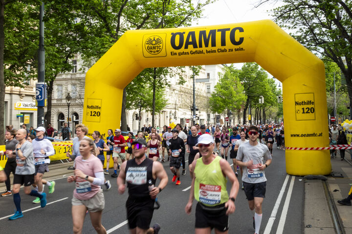 Läufer:innen auf der Strecke beim Vienna City Marathon laufen durch den gelben ÖAMTC Torbogen