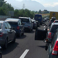 Stau auf einer Autobahn, viele Autos stehen auf beiden Fahrspuren in der Sonne. Im Hintergrund Landschaft mit Bäumen.