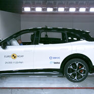 Das Foto zeigt ein weißes Auto von der Seite, das gerade im Zuge eines Crashtests frontal gegen ein Hindernis prallt.